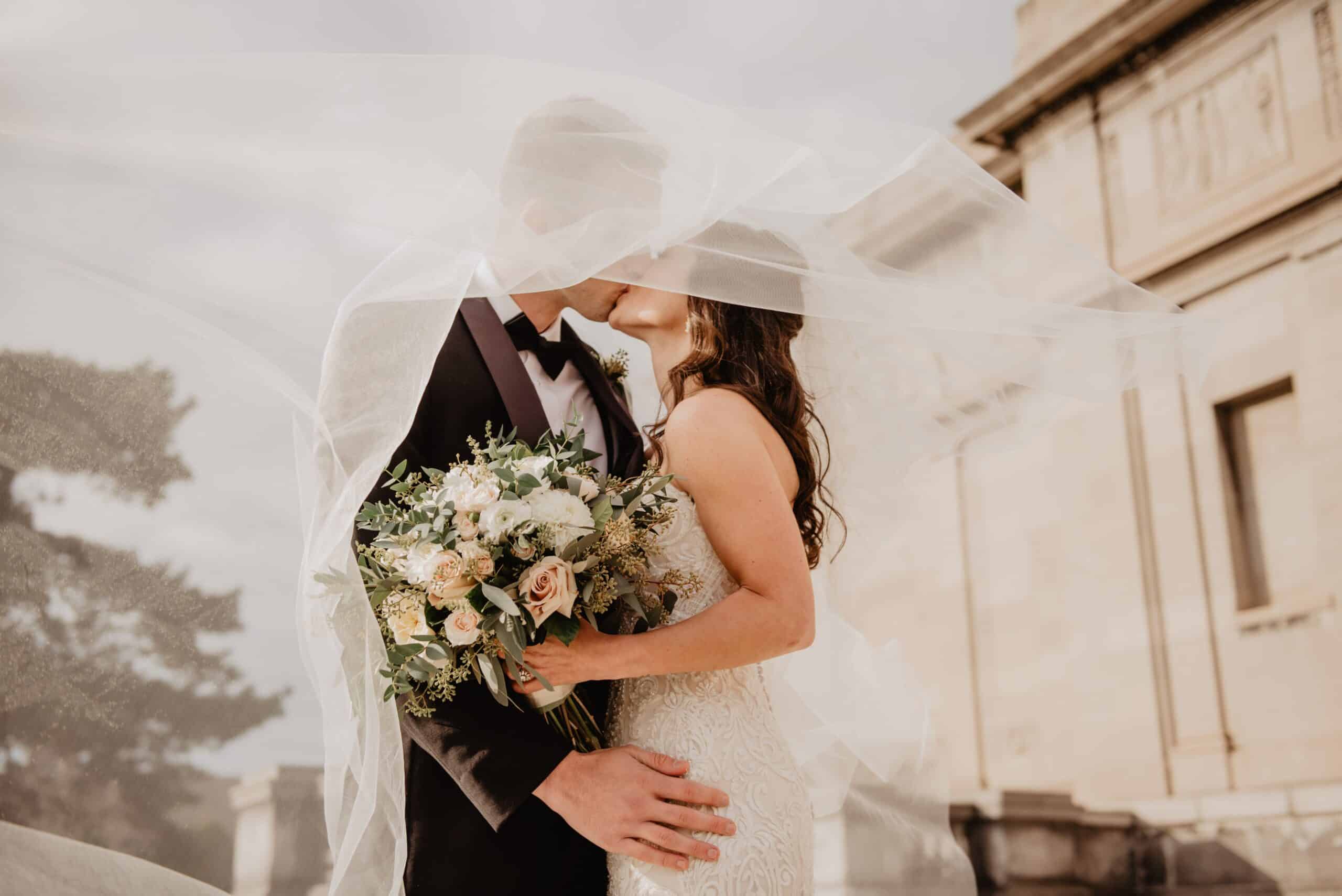 Casal recém casado se beijando com um buquê de flores em mãos